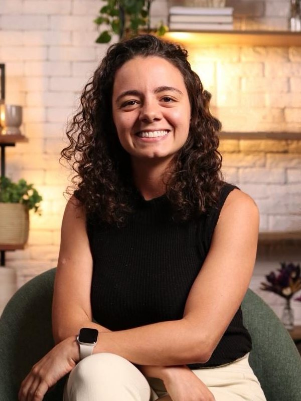 Júlia Benzaquen, sorrindo, sentada numa poltrona